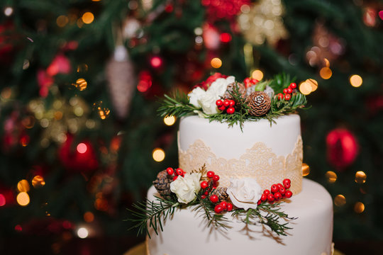 Wedding cake decorated with cones, pine, flowers and berries at winter reception on the background of Christmas tree