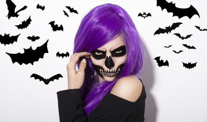 Portrait of woman with terrifying halloween makeup and purple wig over white background. Flying bats