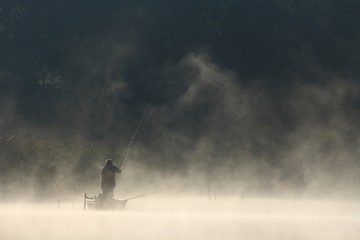 Man in boat fishing on the lake in misty morning 