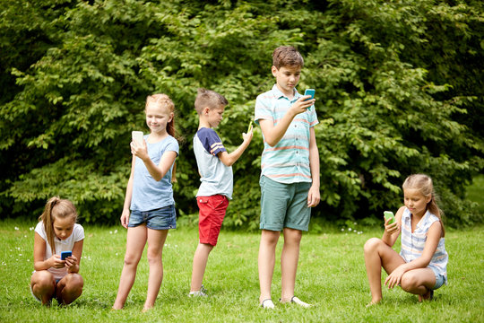 Kids With Smartphones Playing Game In Summer Park