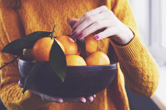 Girl at home holding wooden bowl full of ripe winter tangerines