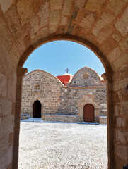 Fototapeta na wymiar View of the old Orthodox Church (1060) of the Assumption of the Virgin Mary through the arch of the bell tower. Asklipio, Rhodes, Greece