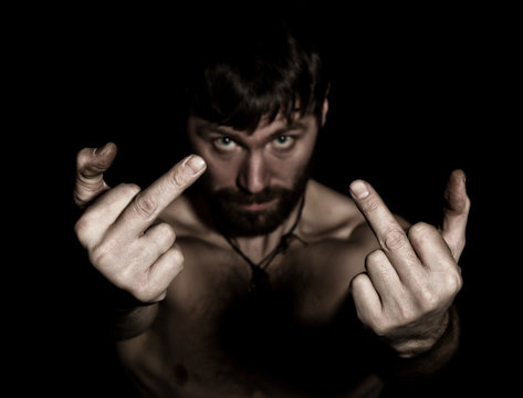 Dark portrait of scary evil sinister bearded man with smirk, showing middle finger. strange Russian man with a naked torso