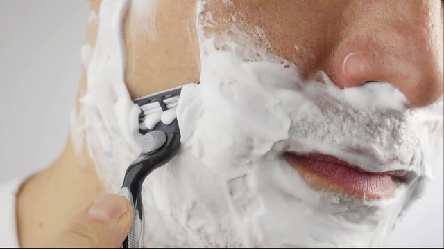 Man shaving with foam and manual razer. Close up of man shaving beard.