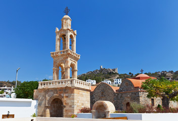 Obraz premium Asklipio. Rhodes. Greece. Bell tower and Church of the Assumption of the Virgin Mary (built at 1060). On the mountain can be seen the ruins of a medieval knight's castle