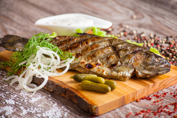 Grilled trout on a wooden board with lemon, pickles and sauce. d