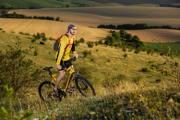 Fototapeta premium Young cyclist on a rural road through green spring meadow
