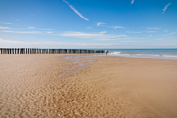 On Bleriot Plage, France a distant figure walks alone under a blue sky.