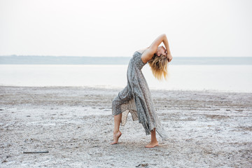 Pretty young woman in dress dancing barefoot on the beach