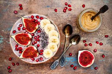 Healthy fall and winter breakfast set. Acai superfoods smoothies bowl with chia seeds, pomegranate, sliced banana, fresh figs and hazelnut butter. Overhead, top view.