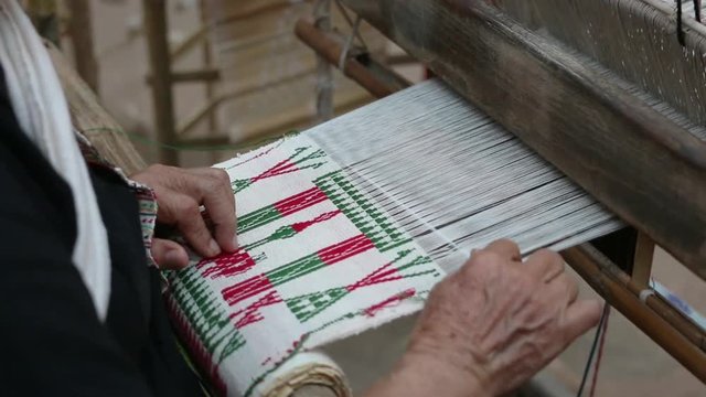 Old woman weaving white red and green cotton flag pattern on loom
