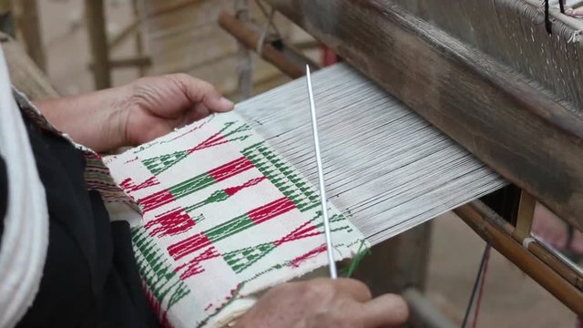 Old woman weaving white red and green cotton flag pattern on loom
