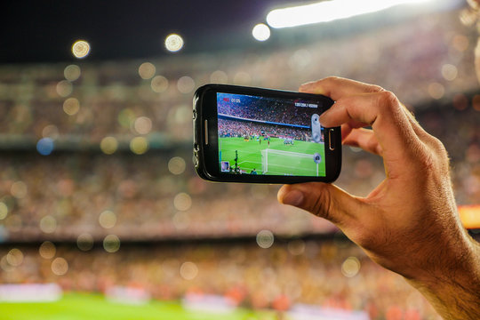Supporter football team recording goal with mobile phone camera.