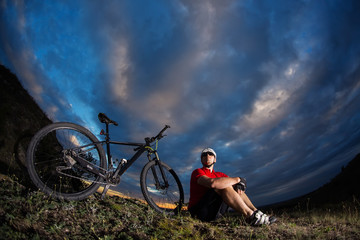 Cyclist resting on grass in mountains. Man is looking aside.