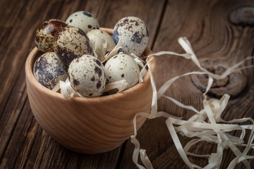 Raw quail eggs in a wooden bowl on wooden table.
