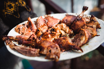 man's hand holds grilled roast chicken on white plate