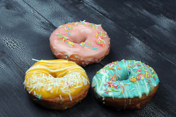 Fresh tasty donuts in soft colorful glaze on a black and white grunge  wooden background
