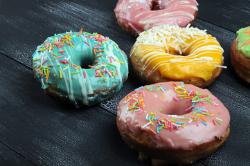 Fresh tasty donuts in soft colorful glaze on a black and white wooden background
