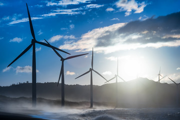 Wind turbine power generators silhouettes at evening ocean coastline. Alternative renewable energy production in Philippines