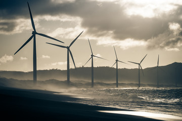 Wind turbine power generators silhouettes at ocean coastline at sunset. Alternative renewable energy production in Philippines