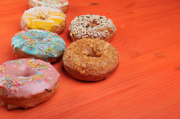Fresh tasty donuts in soft colorful glaze on a orange wooden background