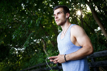Sports muscular guy with headphones in park