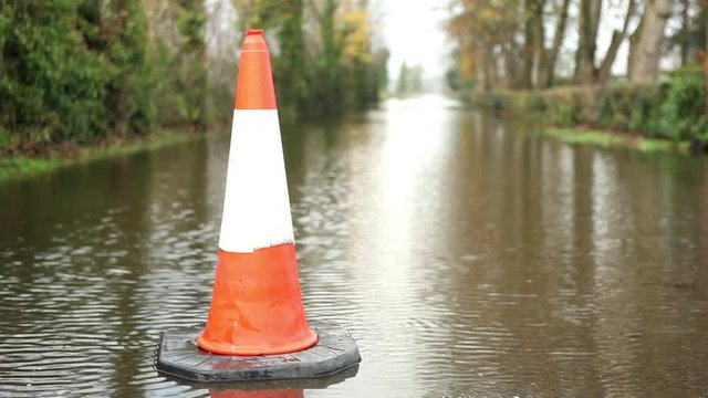 Floods after storm, heavy rain, traffic cone warning on flooded road