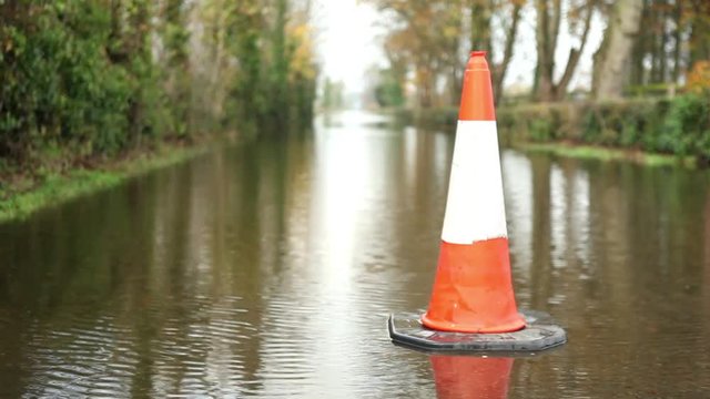 Floods after storm, heavy rain, traffic cone warning on flooded road