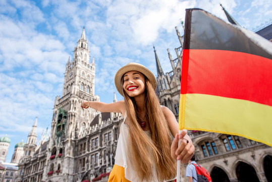 Portrait of a young female tourist with german flag standing on the central square with town hall building on the background in Munich. Having a great vacation in Germany