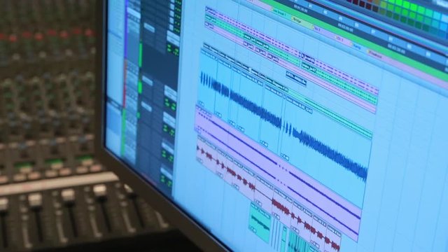 Close up a digital audio workstation with multiple tracks in a music studio.