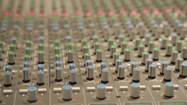 Slow close up pan of knobs on a large audio console in a music studio.
