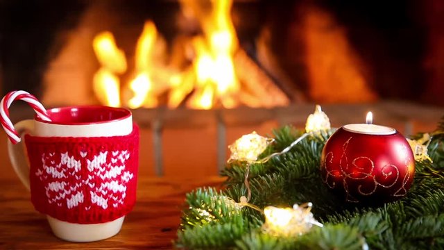 Cup of mulled wine and Christmas tree decoration near fireplace