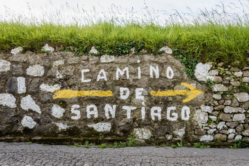Grosser gelber Pfeil und Aufschrift Camino de Santiago auf Mauer am Wegrand am Jakobsweg in Spanien
