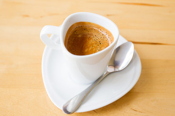 Hot espresso in white cup on wooden table close up.