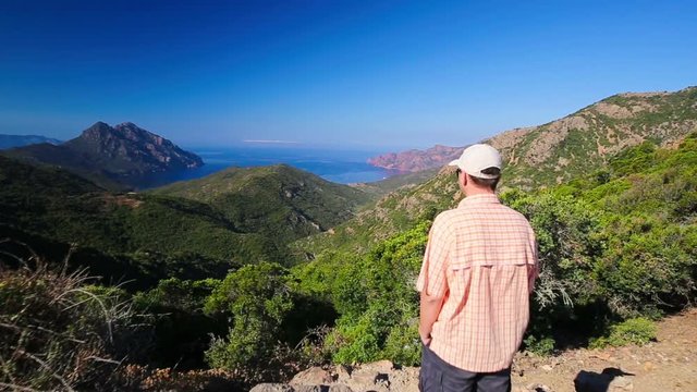 Young attractive man enjoying the view from famous D81 coastal road with view of Golfe de Girolata from Bocca Di Palmarella, Corsica, France, Europe
