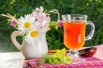 Бокал с квасом и букет садовых цветов в кувшине на деревянном столе в саду