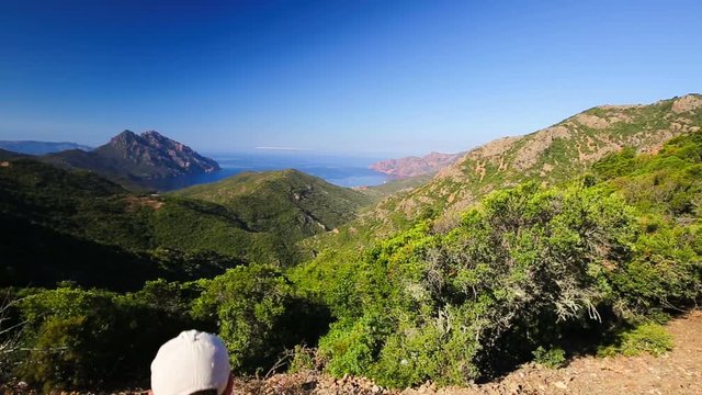 Young attractive man enjoying the view from famous D81 coastal road with view of Golfe de Girolata from Bocca Di Palmarella, Corsica, France, Europe
