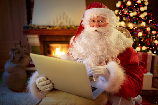 Santa Claus sitting by the fireplace with laptop