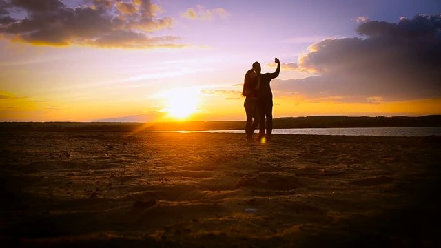 Lovers man and woman in the sunset make selfie against a beautiful sky