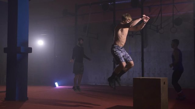 Muscular shirtless man doing twisting backflip jump off the box at the gym in slow motion.