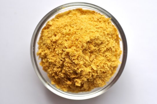 Nutritional yeast in a bowl close-up on white background, top view