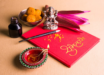 An auspicious Indian writing Shubha Labh means 'Goodness' & 'Wealth', over Red accounting note book / 'bahi khata' with goddess Laxmi, diya, sweets and lotus and pen with ink on laxmi pujan, on diwali © StockImageFactory