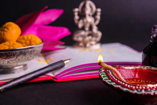 An auspicious Indian writing Shubha Labh means 'Goodness' & 'Wealth', over Red accounting note book / 'bahi khata' with goddess Laxmi, diya, sweets and lotus and pen with ink on laxmi pujan, on diwali