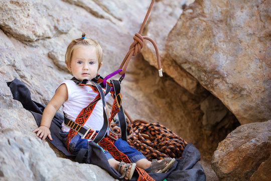 Little Girl Fastened To Rock Climbing Gear And Sitting On Cliff