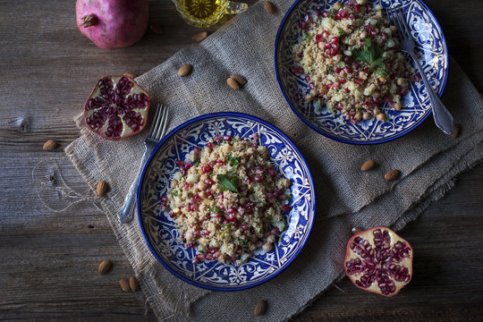 Couscous with chickpeas, almonds and pomegranate on ceramic blue plates and rustic wooden table