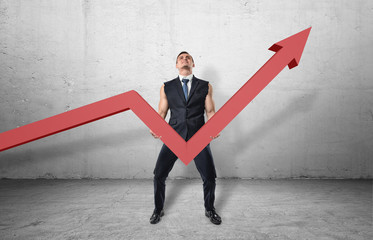 Businessman holding big red line graph with an upturned arrow and trying to raise it up