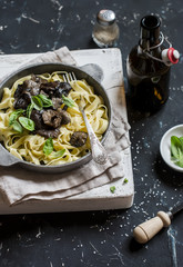 Italian pasta tagliatelle with wild mushrooms in a frying pan and beer on a dark background. Delicious vegetarian food