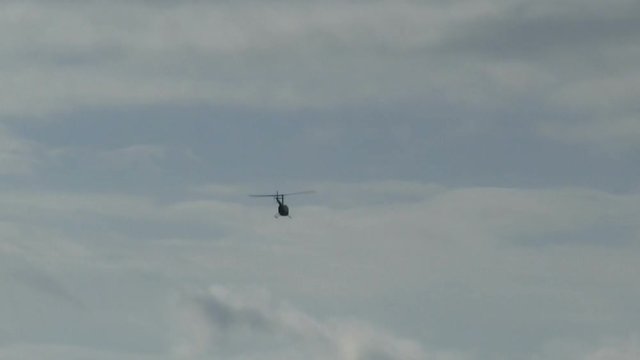 Silhouetted Helicopter Flying Away In White Cloudy Sky
