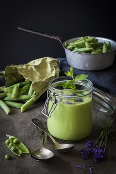 Green gazpacho in jar with peas and lavender on wooden table wit