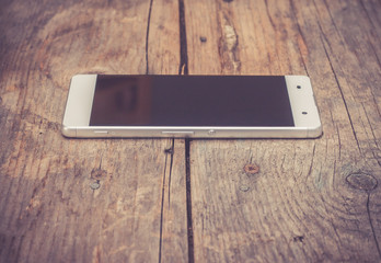 Smartphone mit randlosem Display auf rustikalem Holzuntergrund, Vignettierung